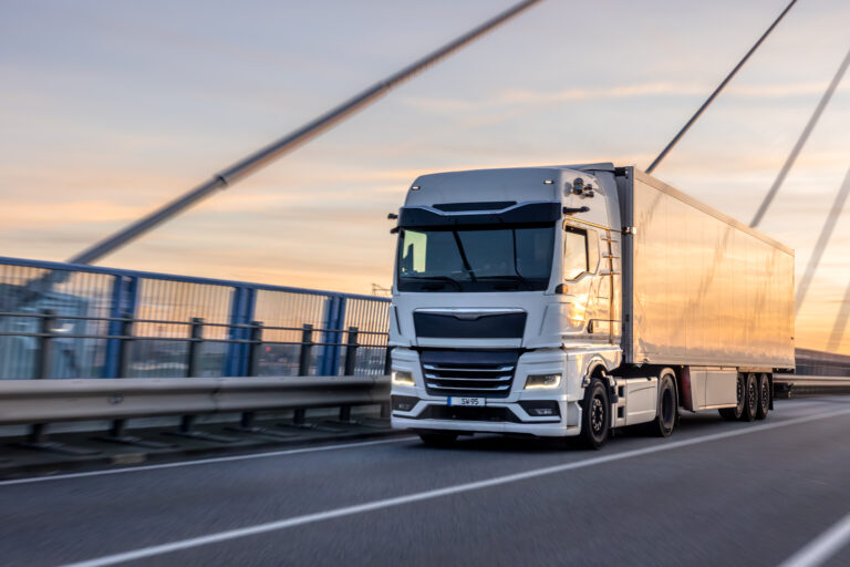 A powerful white freight truck drives over the modern bridge at golden hour. Concept of professional logistics, speed, and efficient transportation at sunset.